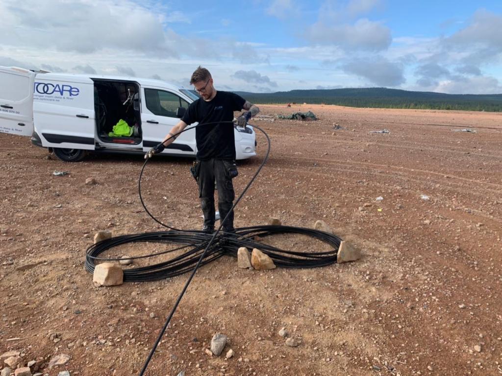 Bilden visar medarbetare som arbetar utomhus med kabel. Företagsbil i bakgrunden.